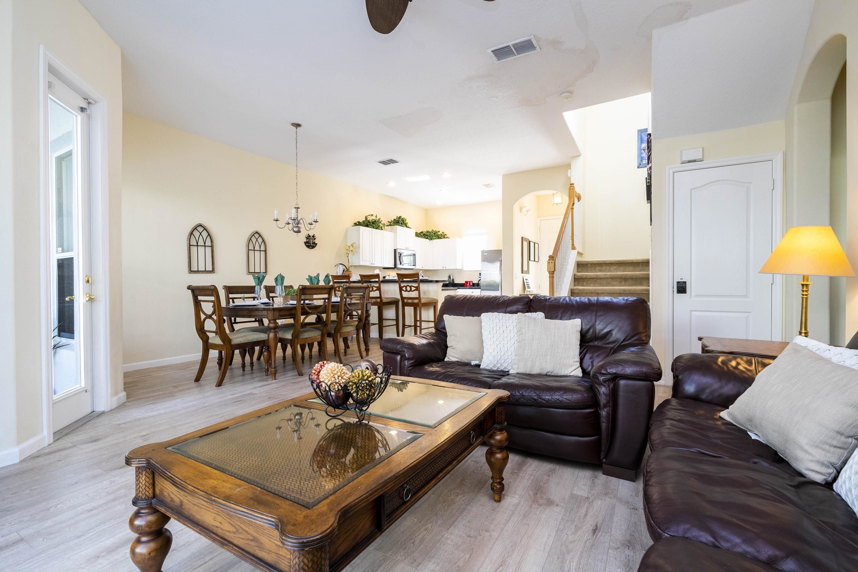 A living room with a dark brown leather sofa, a wooden coffee table, and a dining area with wooden chairs and a table.