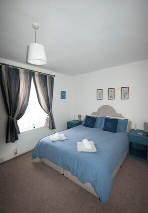 A bedroom with a bed, nightstands, a window with curtains, and wall art.