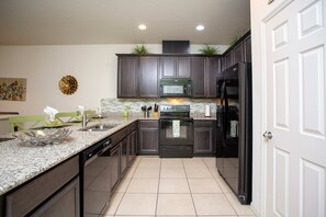 A kitchen with dark cabinets, a microwave, a refrigerator, and a dishwasher. - Family Friendly 4 Bd w GameRoom near Disney 5103 (Kissimmee)
