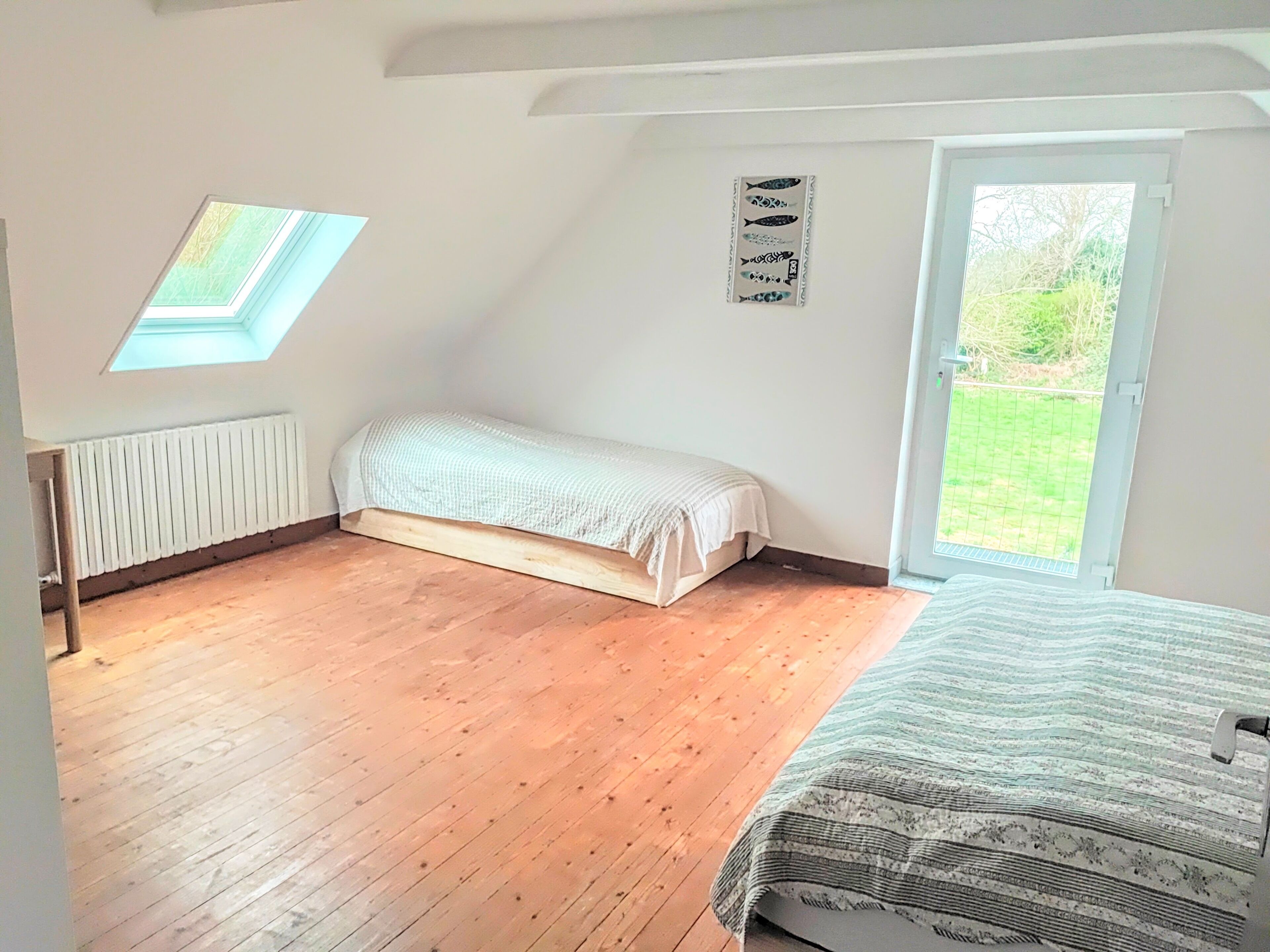 Ein Schlafzimmer mit Oberlicht, Bett, Heizkörper und einer Tür, die in einen Garten führt.