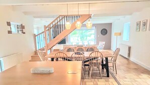 Comedor con mesa y sillas de madera, una escalera y vistas al exterior.