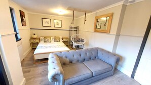 A bedroom with a bed, a grey sofa, a hanging chair, and a mirror on the wall. - Luxurious studio room in the heart of East Kilbride 10mins from a hospital (East Kilbride)