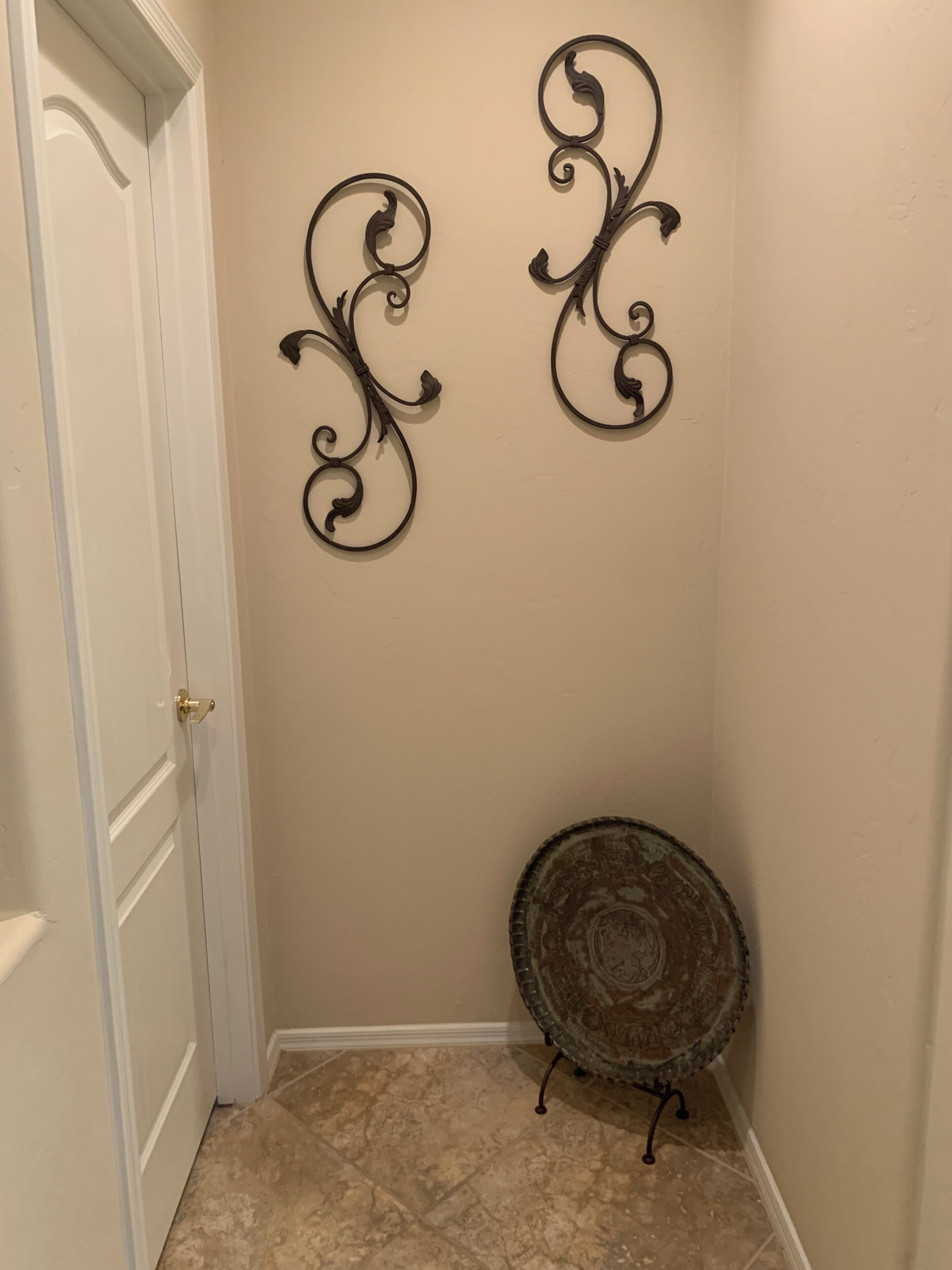 A hallway with a white door, beige walls, and a decorative metal wall piece.