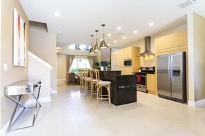 A modern kitchen with a central island, stainless steel appliances, and a dining area with wooden chairs. - Gorgeous 4 Bd Close to Disney   Magic Village 3114 (Kissimmee)