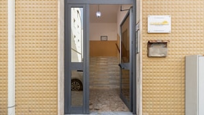 Entrada de hotel com parede texturizada, porta, escadaria e uma placa indicando 'SUMMERTIME HOUSE'.