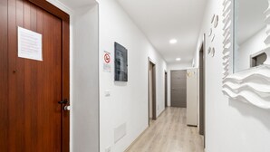Um corredor com uma porta de madeira, um aviso de proibido fumar e um interruptor na parede.