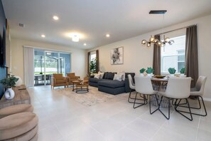 A modern living room with a sofa set, dining table, and chairs, a staircase, and a large window with curtains. - Gorgeous 6Bd w  Pool   Windsor Island 4450 (Davenport)