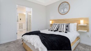 Quarto com cama, mesas de cabeceira, um espelho e porta para o banheiro.