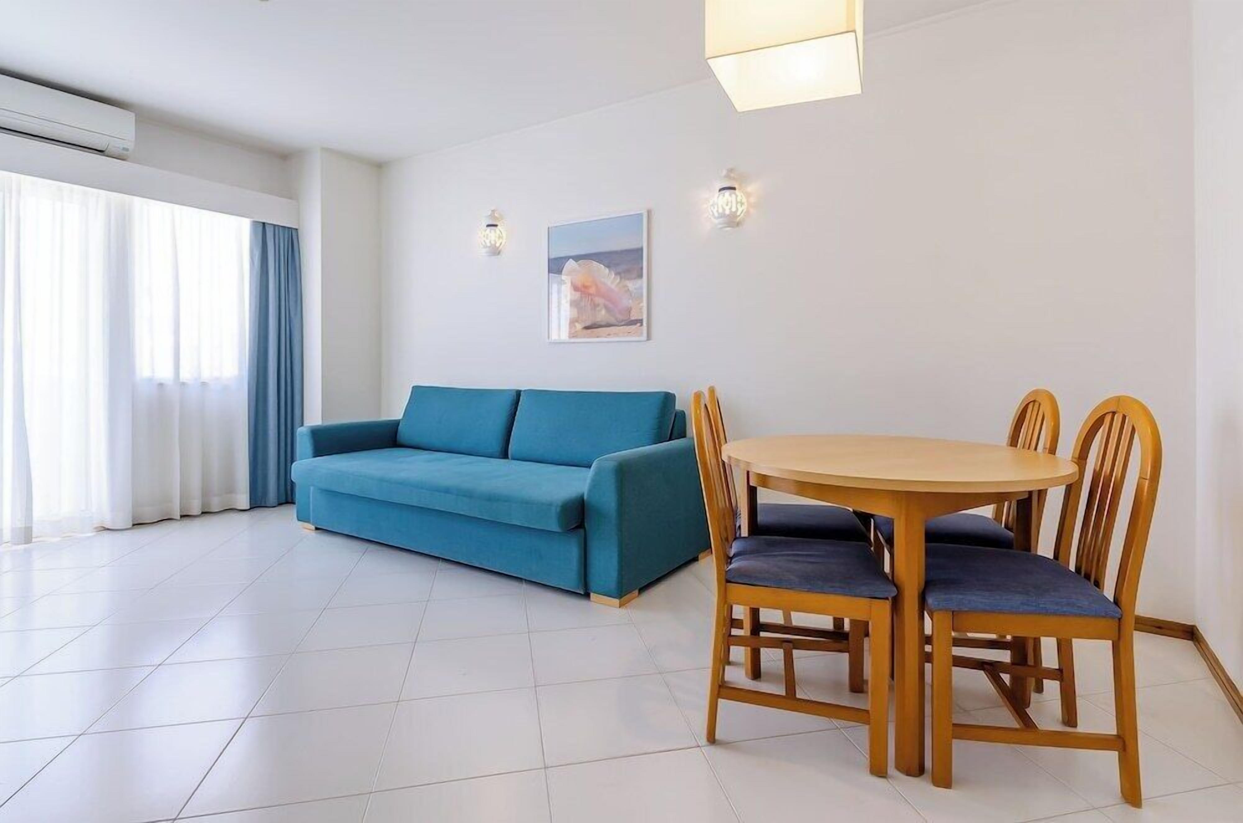 Een moderne woonkamer met een blauwe bank, een houten eettafel met stoelen en een schilderij aan de muur.