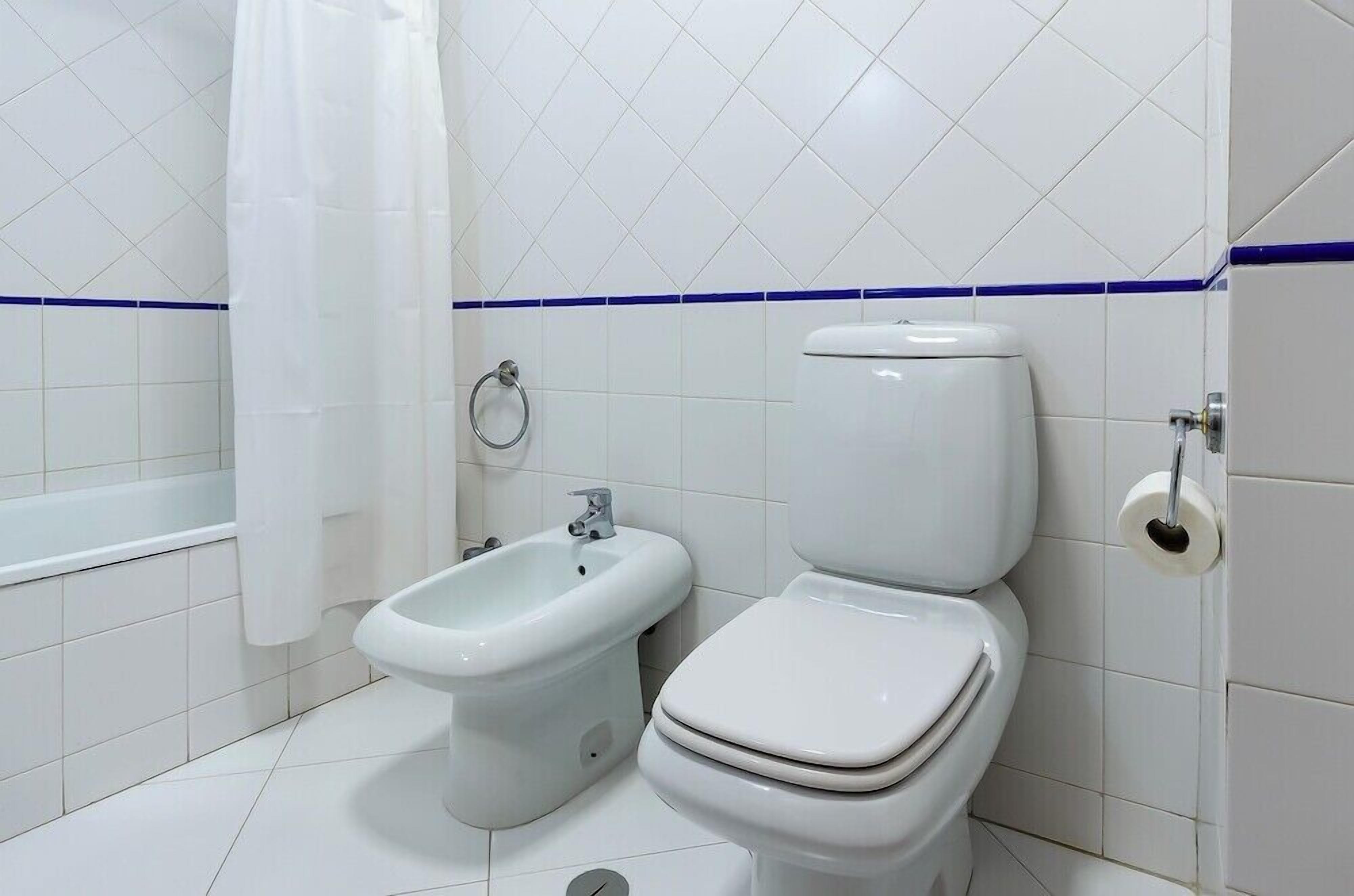 A bathroom with white tiles, a bidet, a toilet, and a bathtub.