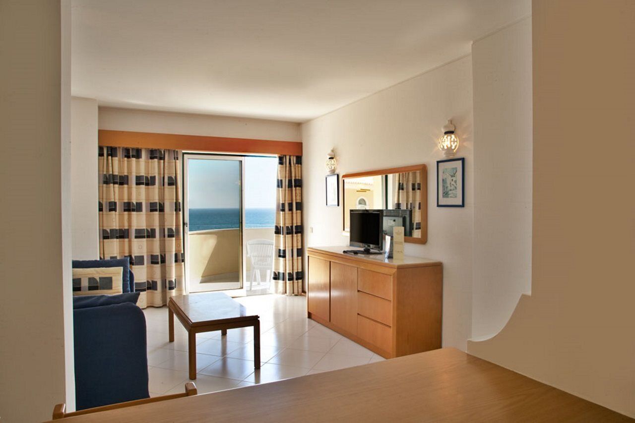 A hotel room with a balcony, a TV, a wooden desk, and a sofa.