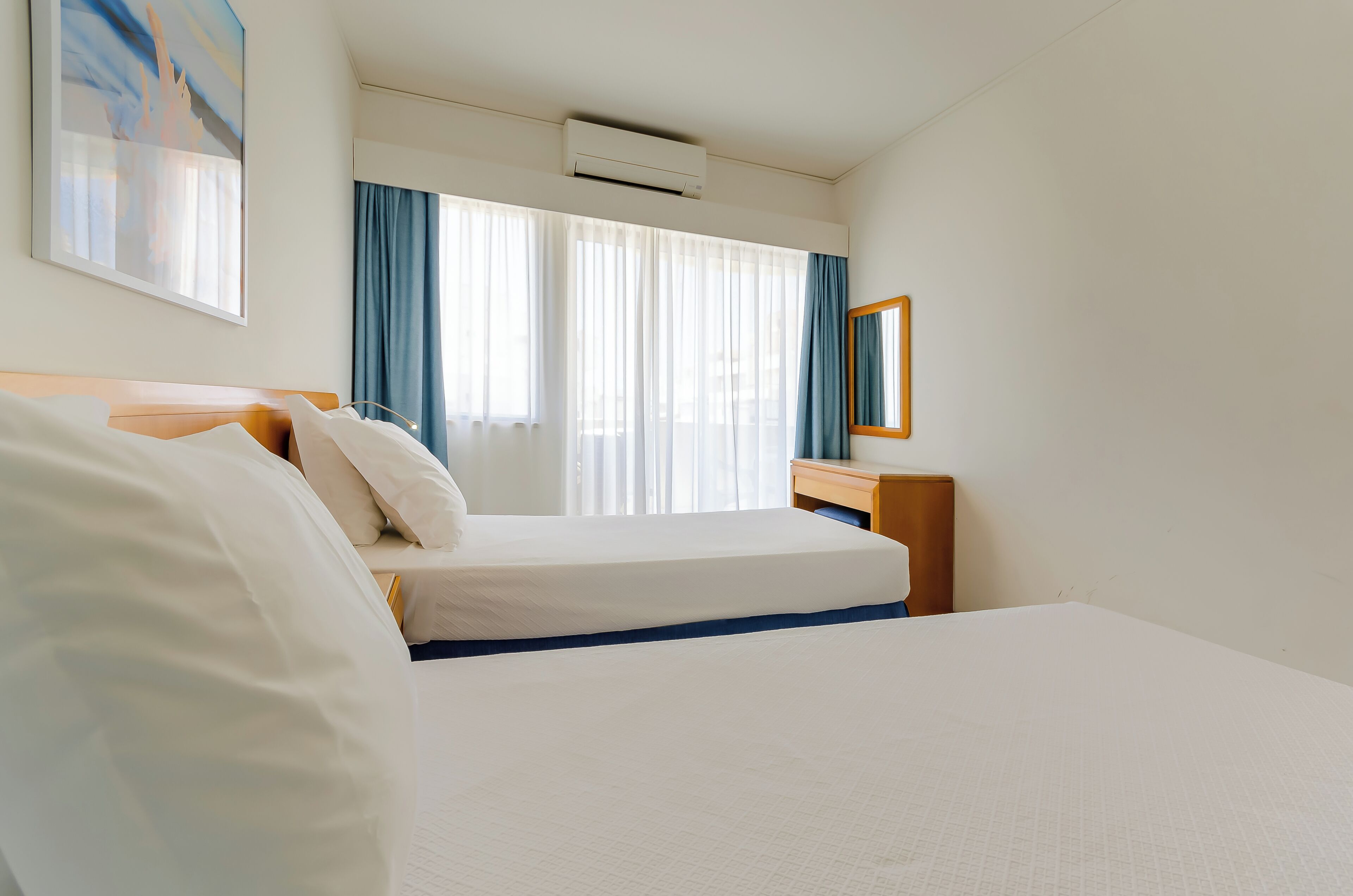 A hotel room with a bed, a desk, a mirror, and a window with curtains.