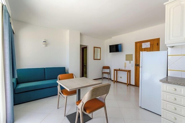 Ein kompakter Wohnbereich mit Sofa, Esstisch, Stühlen, Fernseher, Kühlschrank und Schrank.