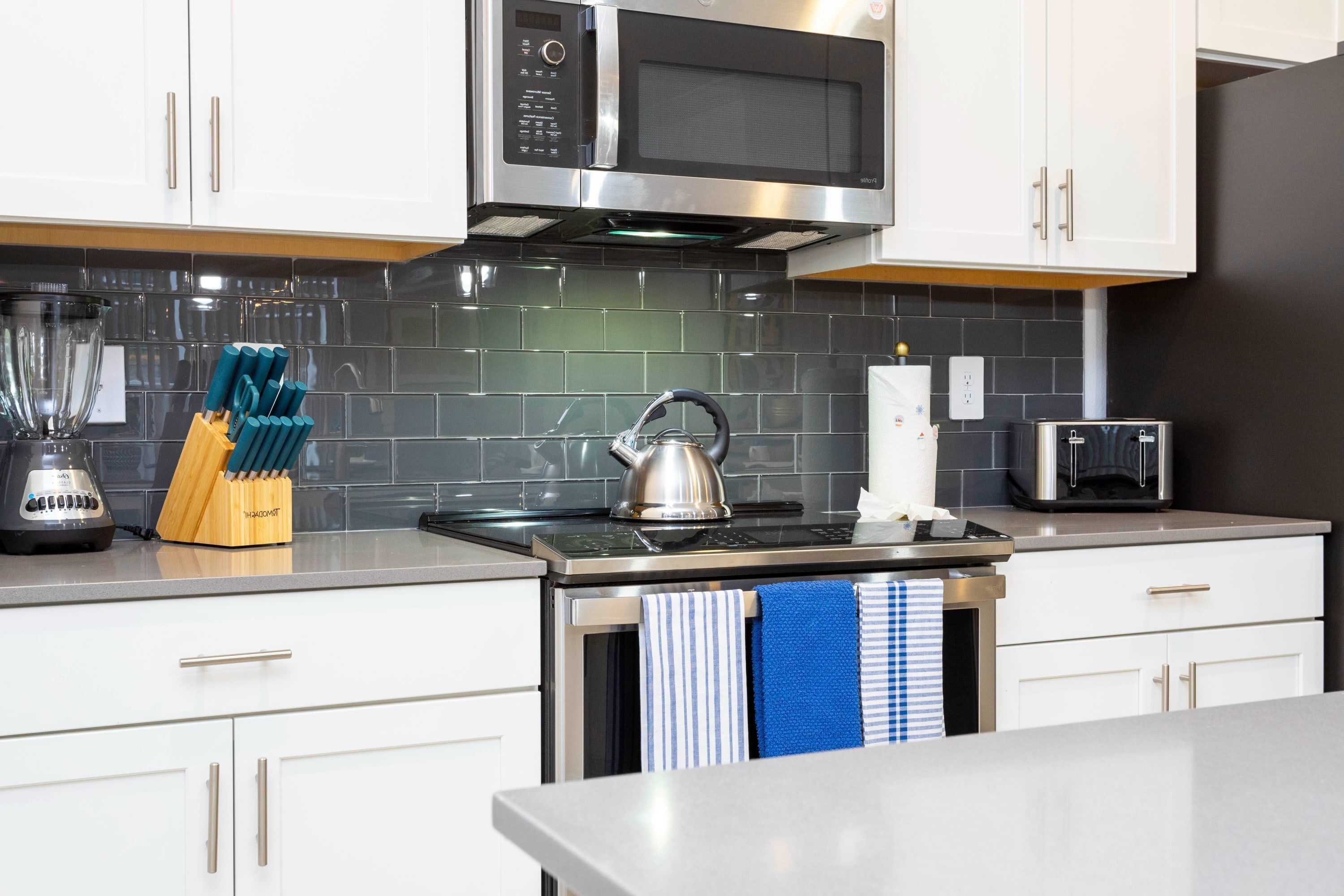 A modern kitchen with white cabinets, a stainless steel microwave, a kettle, and a toaster.