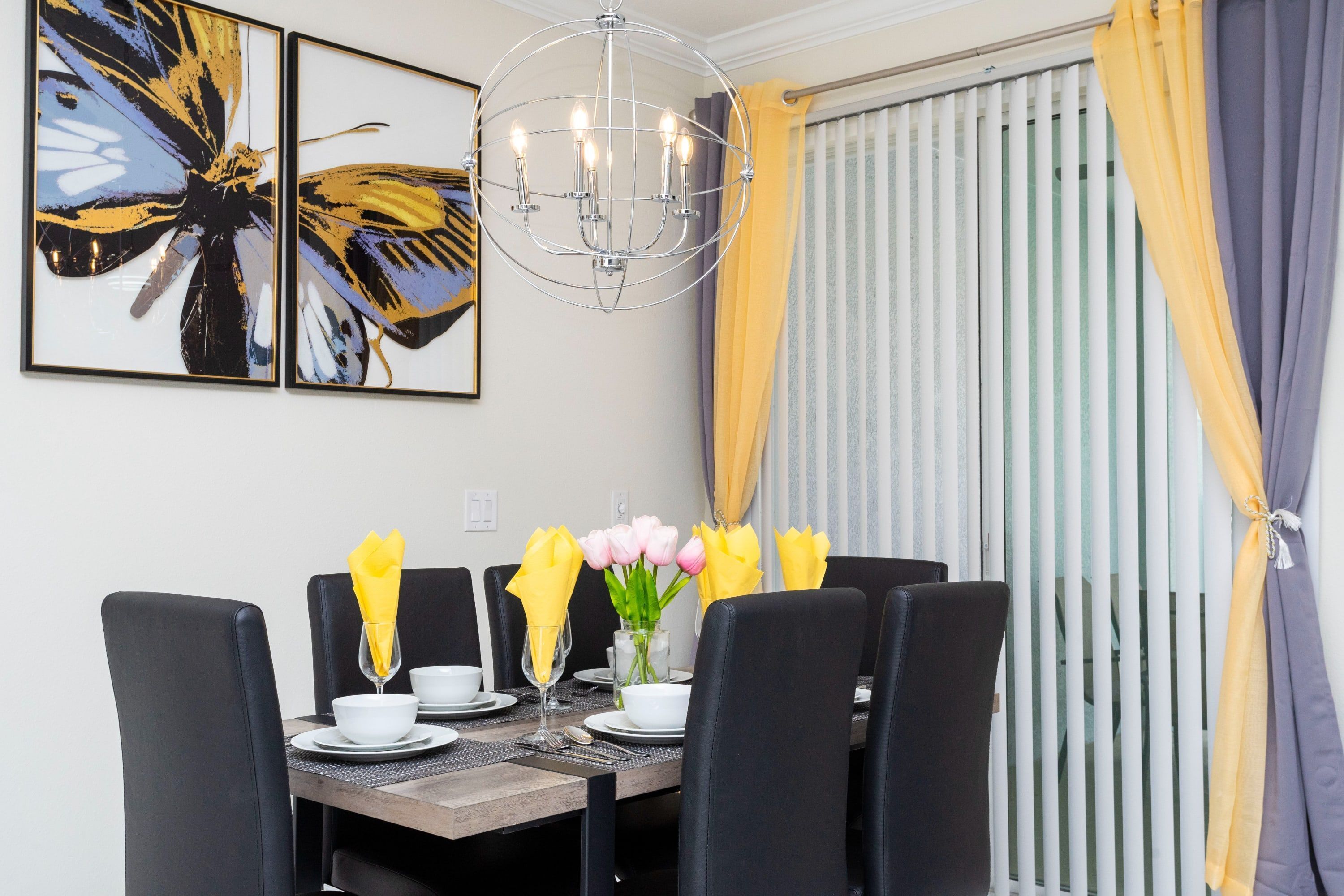 A dining area with a table set for six, black chairs, a chandelier, and artwork on the wall.