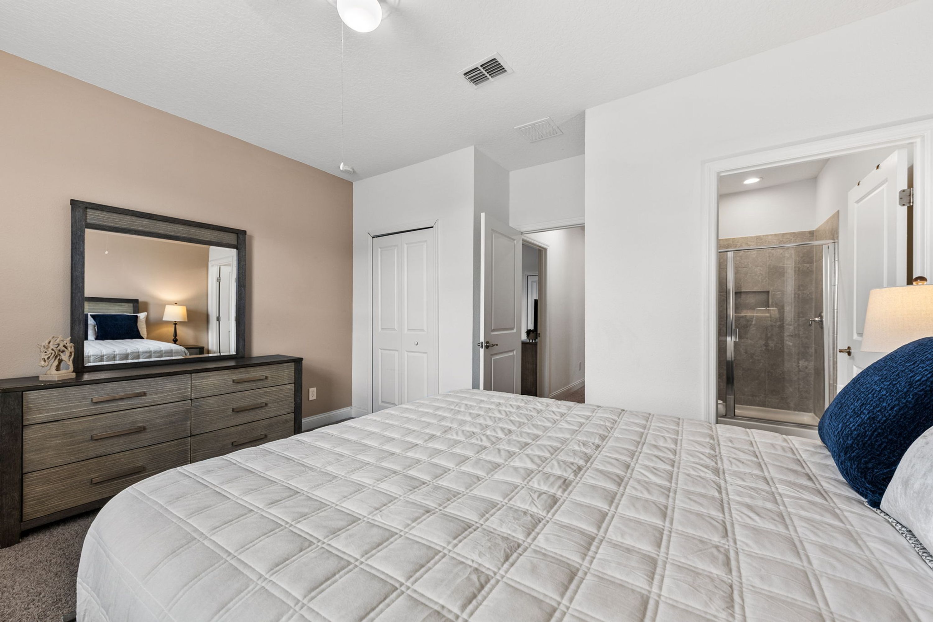 A bedroom with a large bed, a dresser, a mirror, and a door leading to a bathroom.