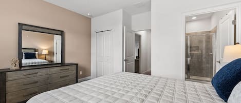 Un dormitorio con una cama grande, un aparador, un espejo y una puerta que da al baño.