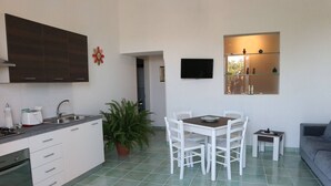 A compact kitchen with white cabinets, a sink, and a dining area with a table and chairs. - Relaxing Escape With the Gods (Agerola)