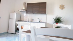 A compact kitchen with white cabinets, a white refrigerator, and a dining area with a white table and chairs. - Relaxing Escape With the Gods (Agerola)