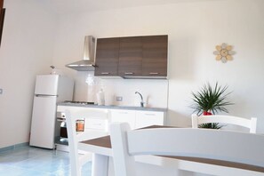 A compact kitchen with white cabinets, a white refrigerator, and a dining area with a white table and chairs. - Relaxing Escape With the Gods (Agerola)