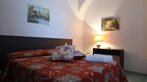 A bedroom with a bed, two paintings, a nightstand with a lamp, and a white towel. - Relaxing Escape With the Gods (Agerola)