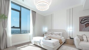 A modern bedroom with a large window, a bed with white bedding, a bedside table, and a small round table with a lamp. - StayShort - Stunning Studio in Business Bay that Sleeps 2! (Business Bay)
