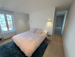 A bedroom with a bed, a nightstand, a bedside lamp, and a view of the outside through a window. - Large modern house in the center of town (Paris)