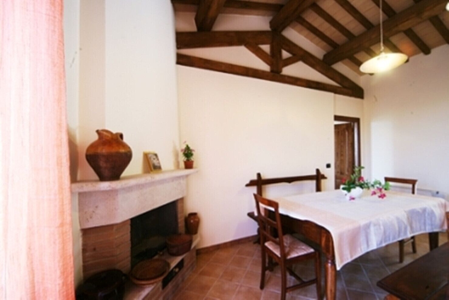 A dining area with a fireplace, wooden chairs, a table with a white tablecloth, and a hanging light fixture.
