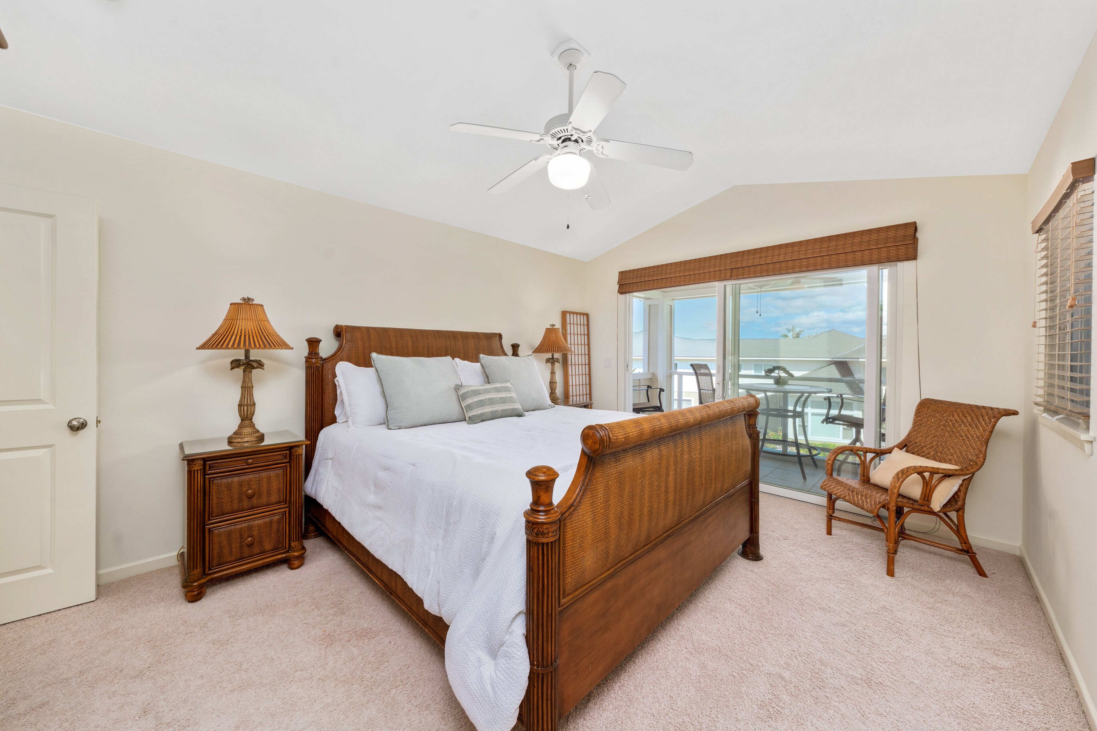 A bedroom with a wooden bed, a nightstand, a chair, a ceiling fan, and a view of the outdoors.