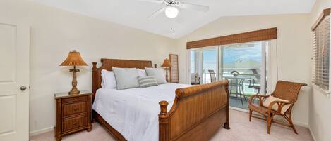 A bedroom with a wooden bed, a nightstand, a chair, a ceiling fan, and a view of the outdoors.
