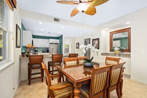 A spacious dining area with a large wooden table and chairs, a ceiling fan, and a kitchen in the background. - Na Hale O Keauhou C6 3 Bedroom Condo (Kailua-Kona)