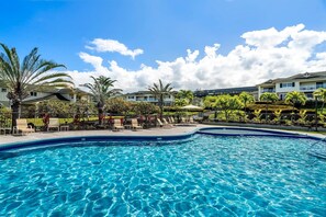 A clear blue swimming pool with lounge chairs and palm trees, surrounded by a fence and buildings in the background. - Na Hale O Keauhou C6 3 Bedroom Condo (Kailua-Kona)