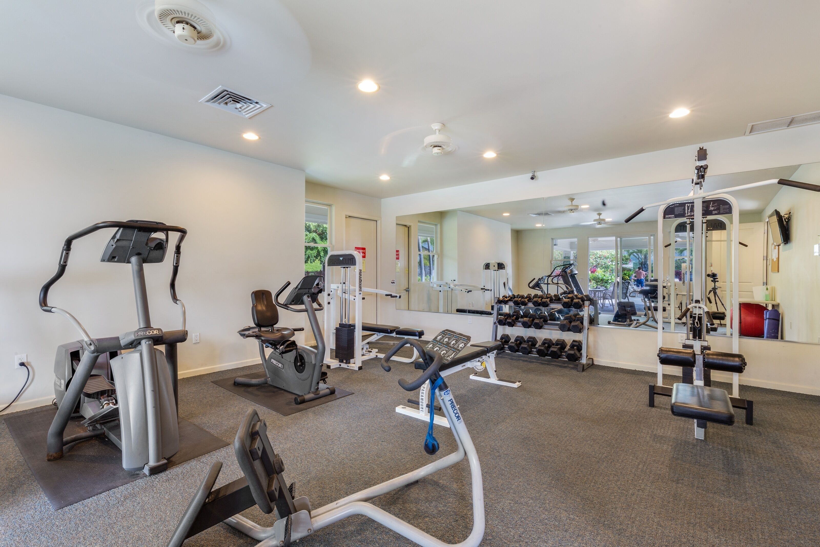 A gym with cardio machines, weightlifting equipment, and a mirror reflecting the room.