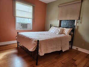 A single bed with a wooden frame and a beige bedspread in a room with wooden flooring and orange walls. - Cozy Church Street Apartment In Historic Galveston 2 Bedroom Apts (Galveston)