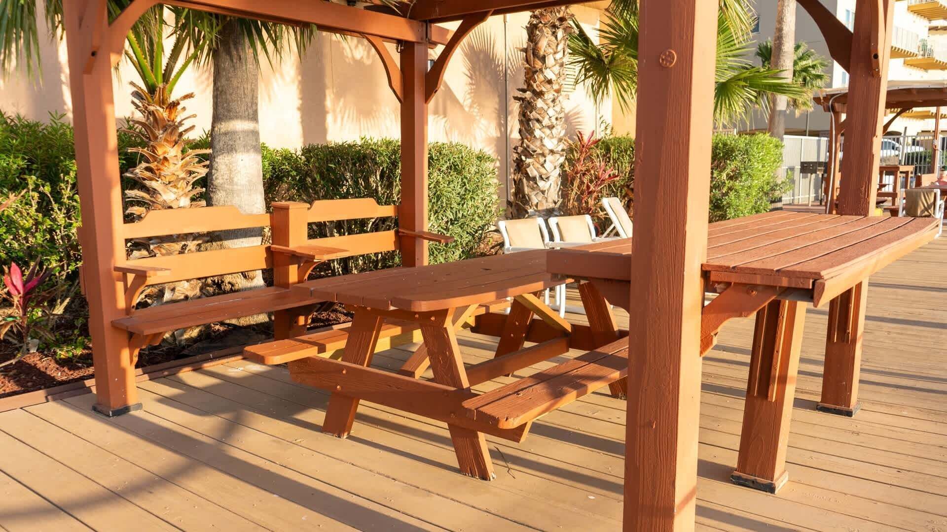 A wooden deck with picnic tables and benches, surrounded by greenery and palm trees.