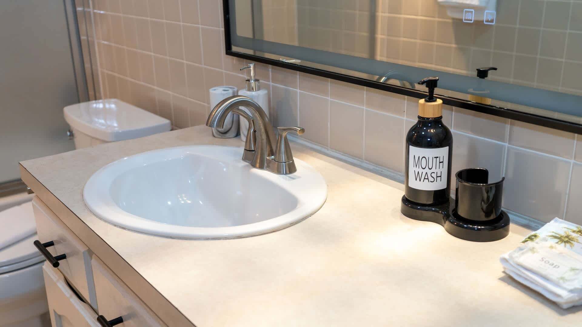 Un baño con lavamanos blanco, grifo, dispensador de jabón y inodoro.