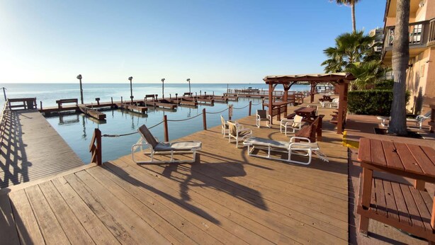 A wooden deck with lounge chairs and a wooden pergola overlooking a calm body of water. - Direct Bayfront Sunsets - Boat Docks - Pool - Fish 2 Bedroom Apts (South Padre Island)