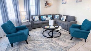 A living room with a grey sectional sofa, two blue armchairs, a coffee table, and a patterned rug. - Direct Bayfront Sunsets - Boat Docks - Pool - Fish 2 Bedroom Apts (South Padre Island)