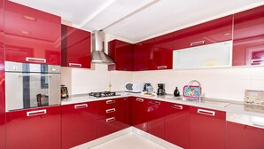 Une cuisine moderne avec des meubles de rangement rouges, des appareils électroménagers en acier inoxydable et un plan de travail blanc.