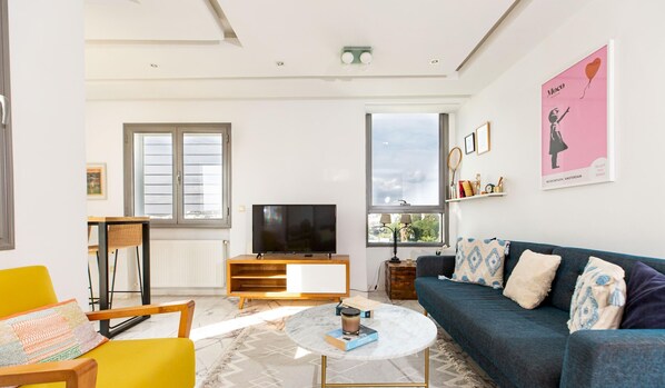 Ein modernes Wohnzimmer mit einer Couch, einem Couchtisch, einem Fernseher und einem Fenster mit Jalousien.