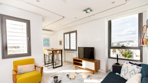 Un salon moderne avec un canapé, un fauteuil jaune, un téléviseur et une table à manger.