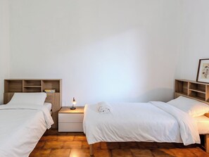 A room with two beds, a nightstand with a lamp, and wooden shelves. - Giardino Bonsai by Interhome (Dervio)