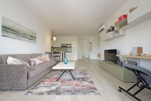 A modern living room with a sofa, coffee table, and TV. There is a kitchen in the background with cabinets and a dining area. - Rifugio incantato sul Tevere (ROMA)