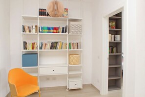 Ein Zimmer mit einem weißen Bücherregal, das mit Büchern gefüllt ist, einer blauen Aufbewahrungsbox und einem Korbwäscher.