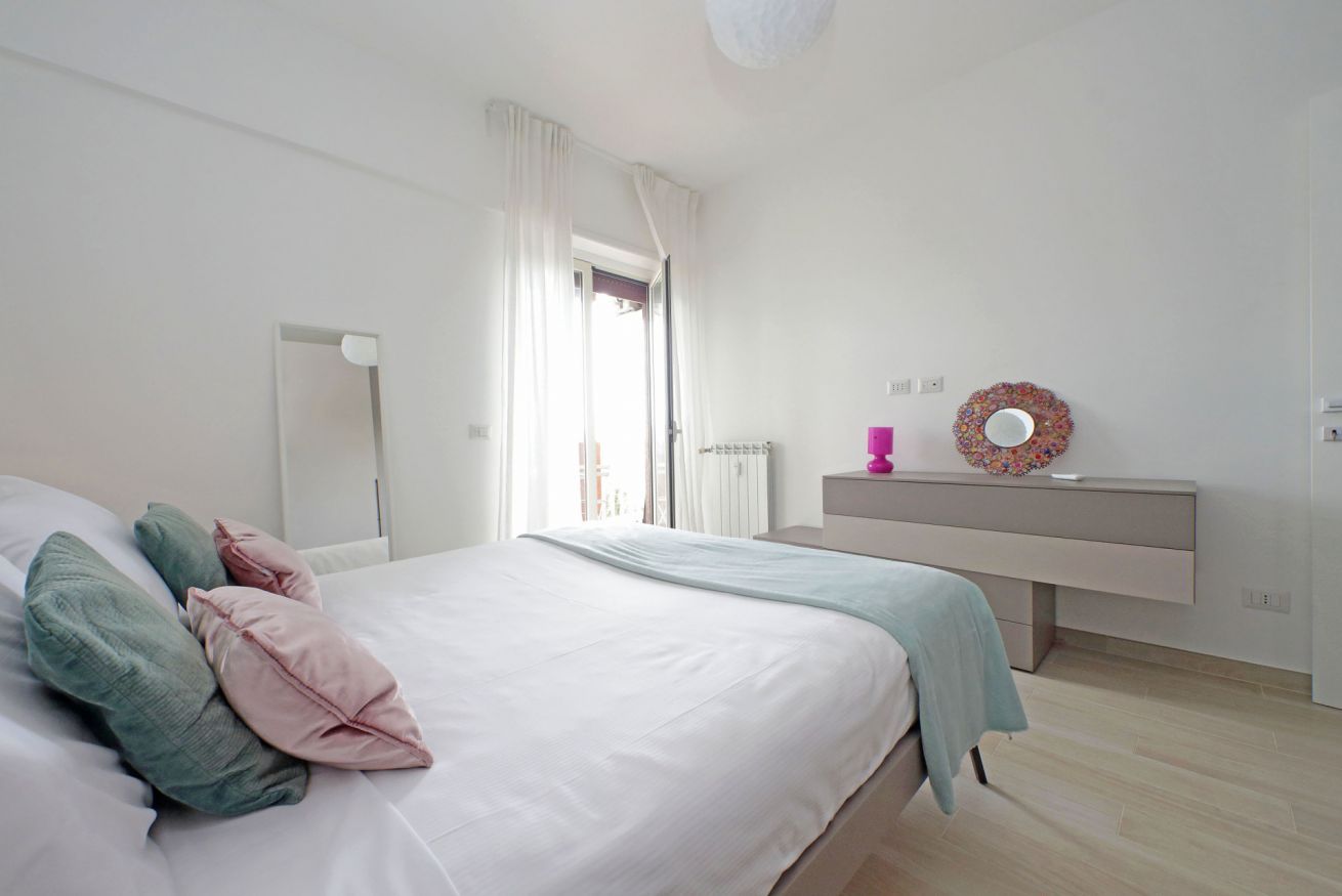 A bedroom with a bed, a bedside table with a mirror, a dresser, and a window with curtains.