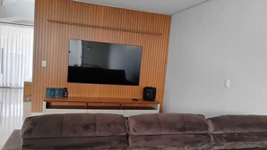 A living room with a large flat-screen TV mounted on a wooden wall, a brown sofa, and a small table with a speaker.
