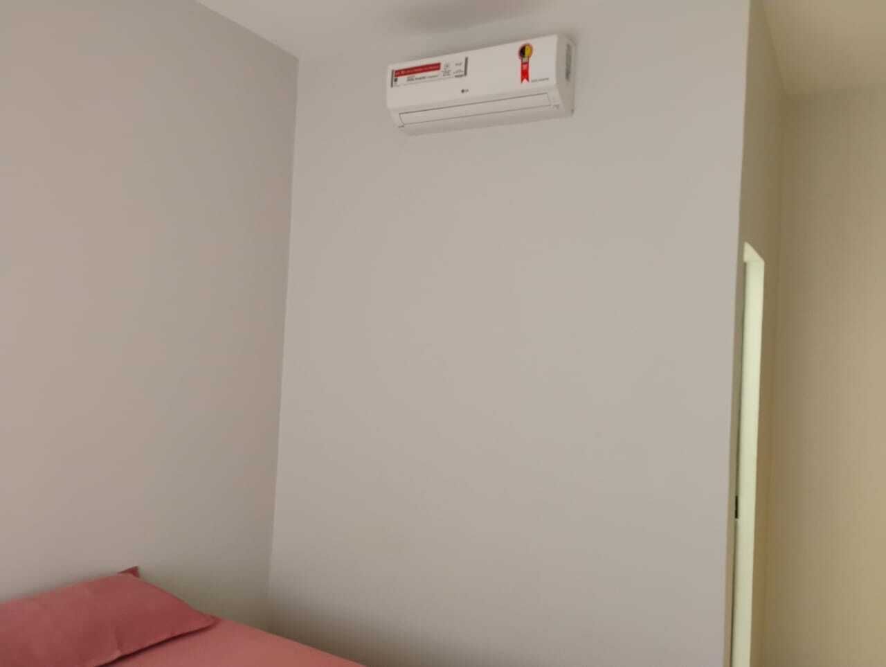 Ein Zimmer mit weißer Wand, einem roten Kissen auf dem Bett und einer weißen Klimaanlage an der Wand.