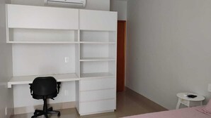 A bedroom with a bed, a desk with a chair, a wardrobe, and a small bedside table.