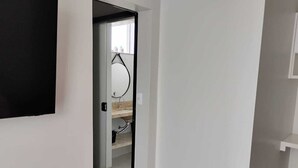 A hallway leading to a bathroom with a shower, a toilet, and a sink.
