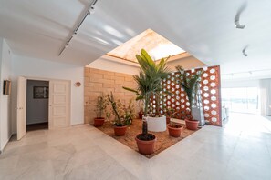 Eine geräumige Lobby mit hoher Decke, Topfpflanzen, einer Backsteinwand und einem Holzlattengitter als Raumteiler.